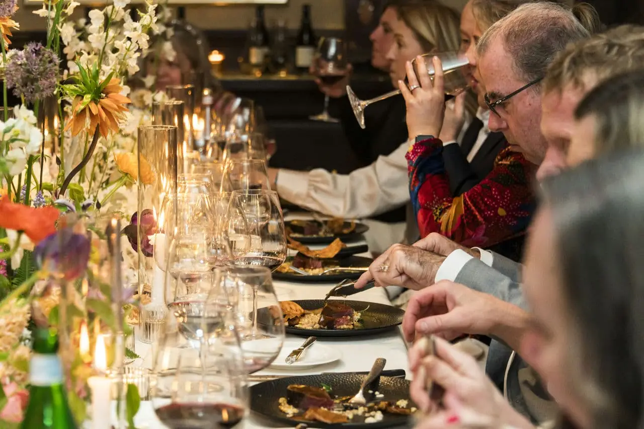 Photograph a row of people eating and drinking wine at an elegant restaurant table