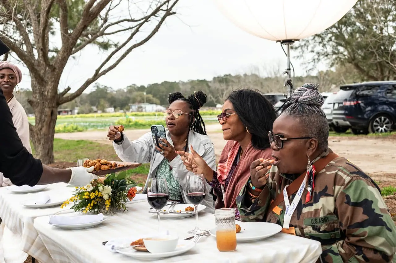 Three women eating and drinking wine outdoors at the Sea Island Cookout event