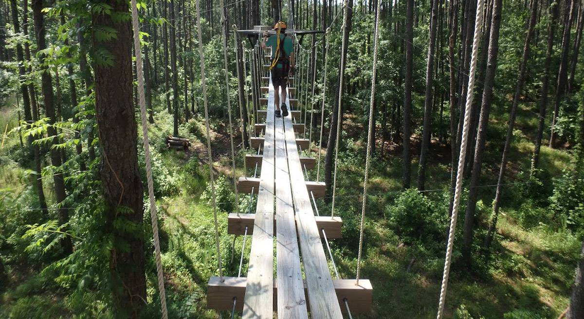 A person crossing a hanging rope bridge in the middle of the forest.